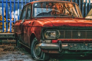 Image of a rusty red car parked next to a fence for the blog How Corrosion Protection Coatings Stop Metal From Rusting